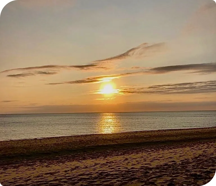 Sunset over the ocean with the sun setting in the sky, casting a warm orange glow over the water