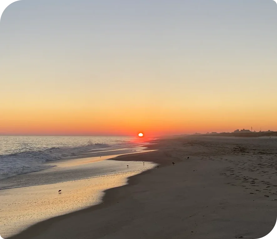 Sunset on the beach with the sun setting in the background, casting a warm orange glow over the water